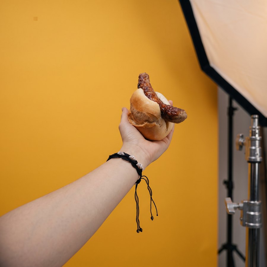 Echte Hand mit Rostbratwurst im Brötchen beim Fotoshooting vor gelbem Hintergrund